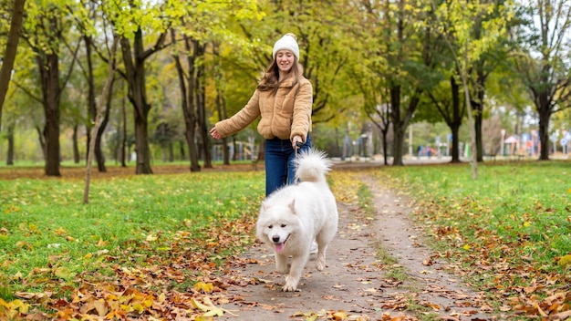 Donna con il suo cane in autunno in un parco. La donna sta camminando e tenendo il guinzaglio. Foglie ingiallite a terra