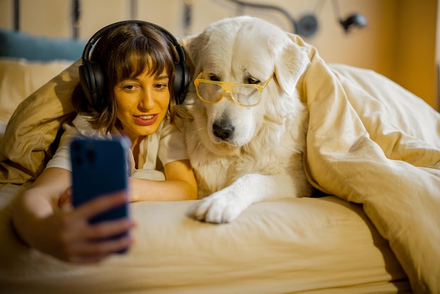 Donna con il suo simpatico cane che usa il telefono a letto