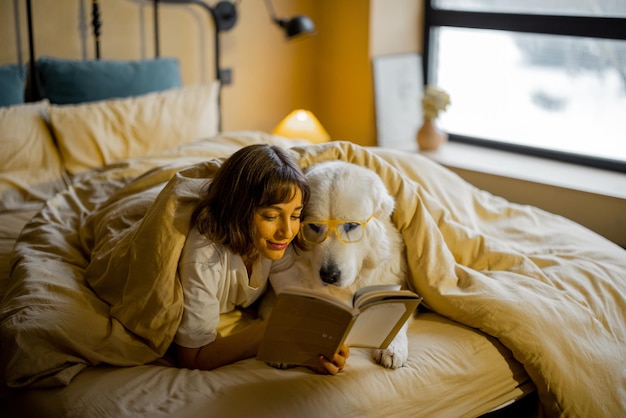 Donna con il suo simpatico libro di lettura del cane a letto
