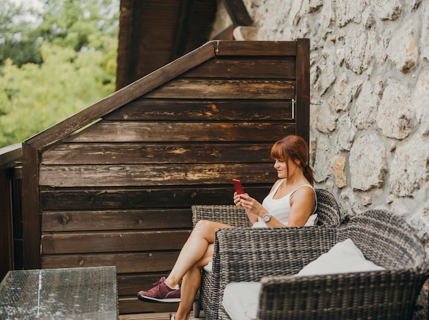 Donna con il suo telefono cellulare seduto sulla terrazza di una camera d'albergo