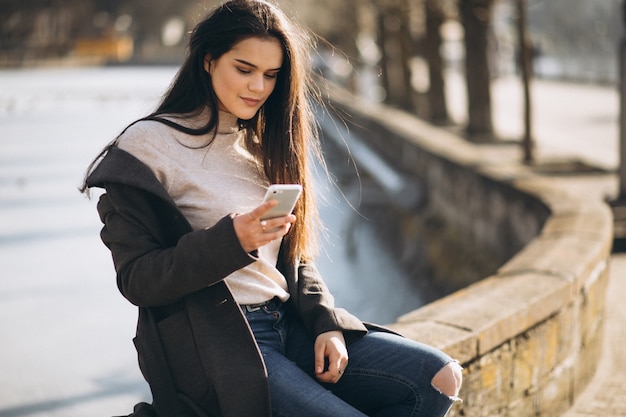 Donna con il telefono che si siede nel parco in inverno