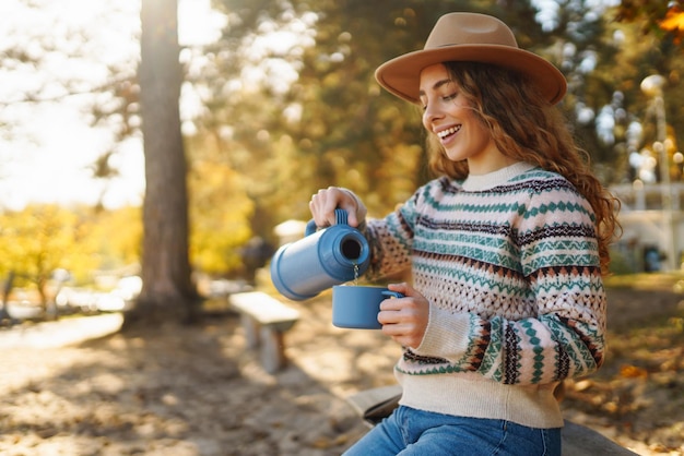 Donna con il thermos e beve tè nella soleggiata foresta d'autunno Concetto di stile di vita di viaggio di vacanza