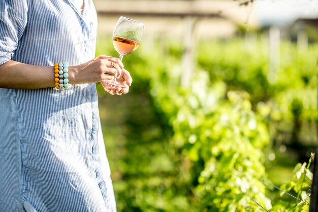 Donna con in mano un bicchiere di vino rosato sullo sfondo del vigneto durante il tramonto