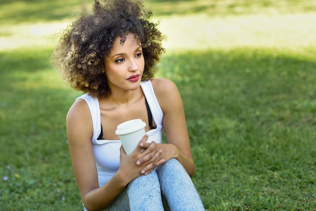 Donna con l&#39;acconciatura afro bere caffè nel parco