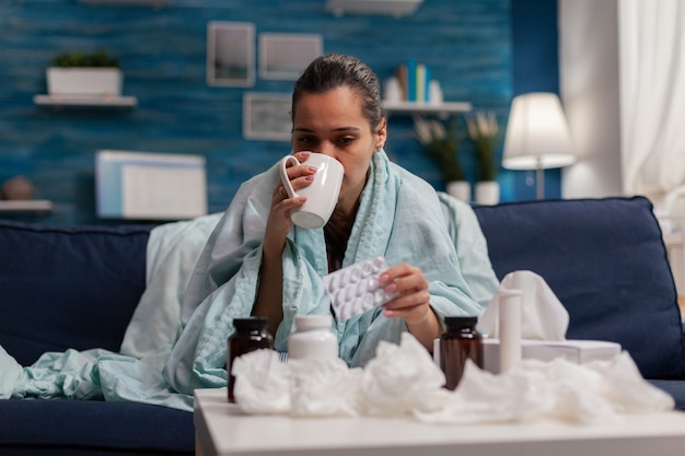 Donna con l'influenza che beve medicine sul divano di casa