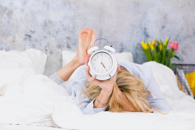 Donna con l'orologio della sveglia mentre giace a letto contro la parete a casa
