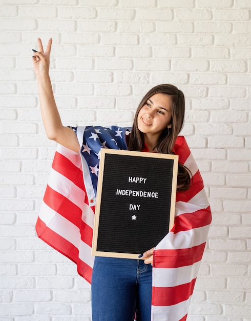 Donna con la bandiera americana che tiene la lavagna con le parole Happy Independence Day e che mostra il segno del pezzo