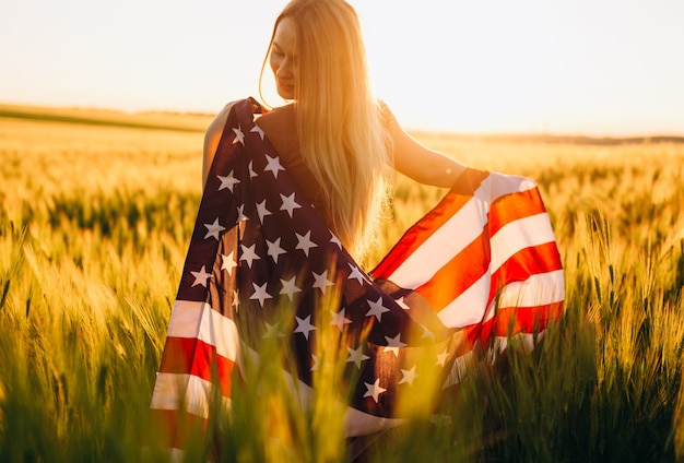 Donna con la bandiera americana in un campo di grano al tramonto