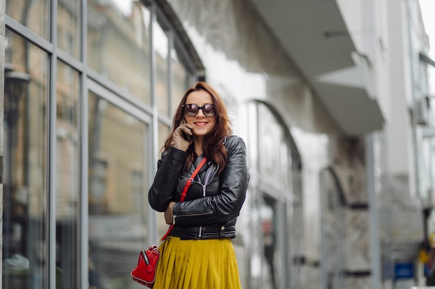 Donna con la borsa rossa che cammina mentre parla al telefono vicino a un edificio commerciale