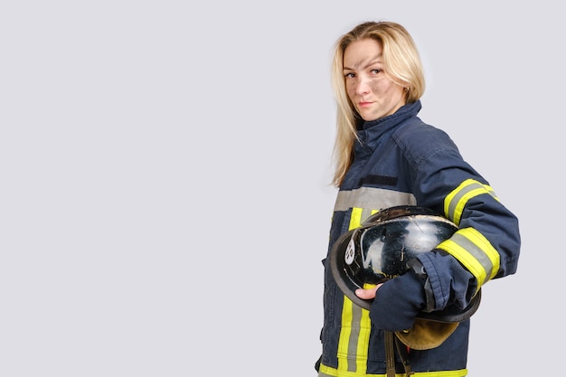 donna con la faccia sporca in uniforme di vigile del fuoco tiene l'elmetto in mano