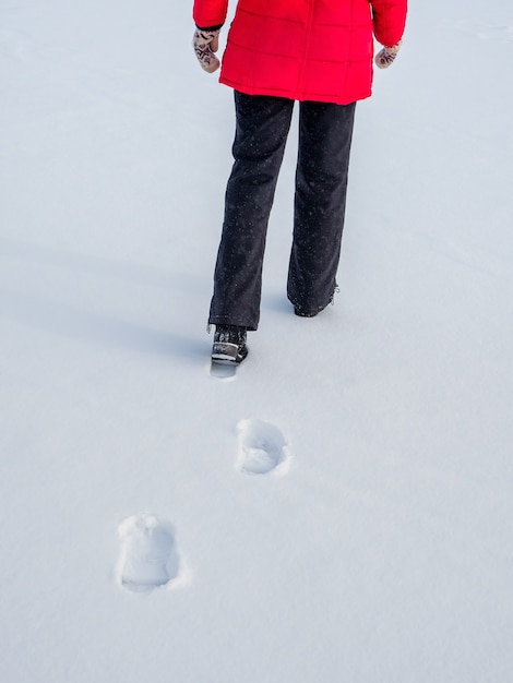 Donna con la giacca rossa che cammina sulla neve, impronte nella neve, dietro.