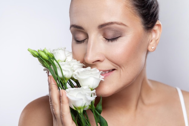 Donna con la pelle pulita dopo le procedure cosmetiche che gode dell'aroma dei fiori con gli occhi chiusi