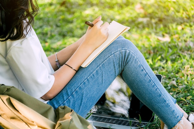 Donna con la penna che scrive su un taccuino che si siede sull&#39;erba nel parco