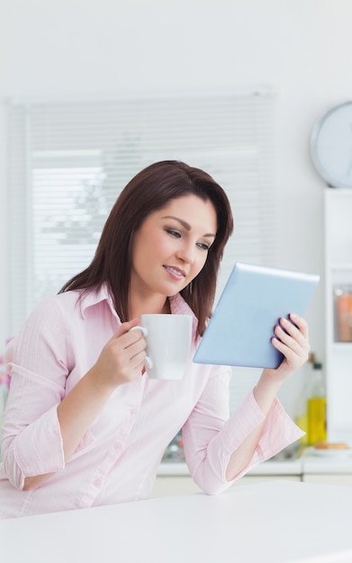 Donna con la tazza di caffè guardando la tavoletta digitale