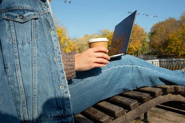 Donna con la tazza di carta e il computer portatile nel parco