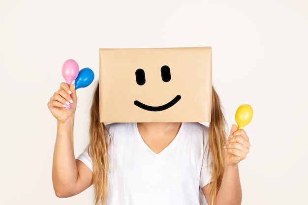 Donna con la testa in una scatola e gesto di sorriso che tiene in mano maracas giocattolo di plastica colorata