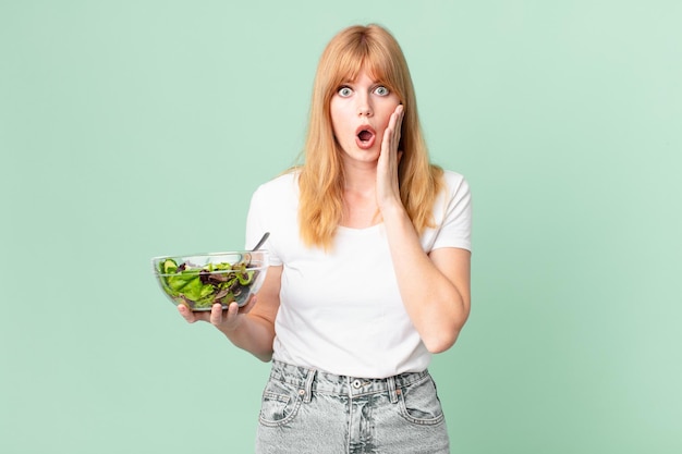 Donna con la testa piuttosto rossa che si sente scioccata e spaventata e tiene in mano un concetto di dieta a base di insalata