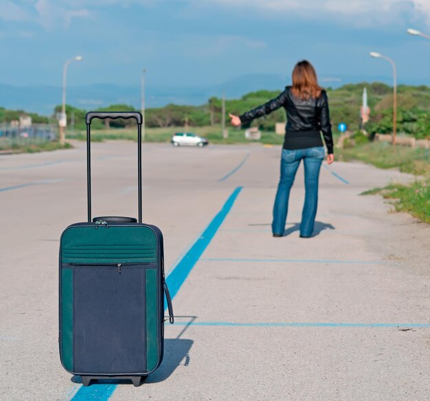 Donna con la valigia che fa l'autostop per strada