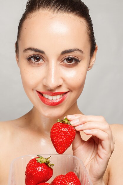 Donna con labbra rosse che tiene il contenitore di plastica pieno di fragole