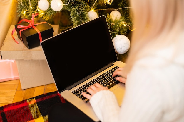 donna con laptop sullo sfondo di un albero di Natale accetta congratulazioni online buon natale