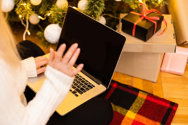 donna con laptop sullo sfondo di un albero di Natale accetta congratulazioni online buon natale