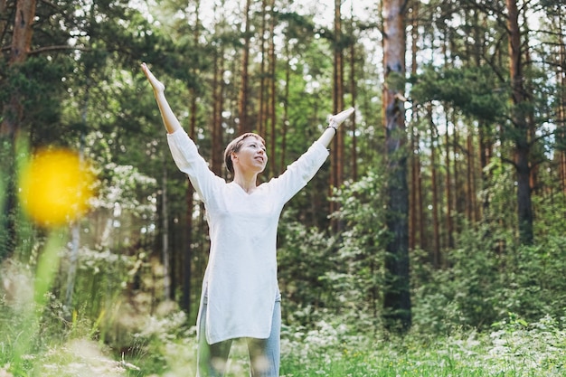 Donna con le braccia alzate in piedi tra gli alberi