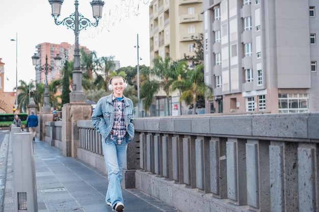 Donna con le cuffie che cammina per la città ascoltando musica e sorridendo Concetto Stile di vita all'aperto in stile urbano