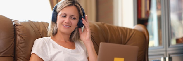 Donna con le cuffie che sorride e guarda lo schermo del laptop mentre è seduto sul divano freelance