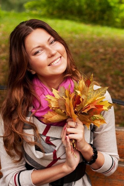 Donna con le foglie di autunno che si siedono sul banco