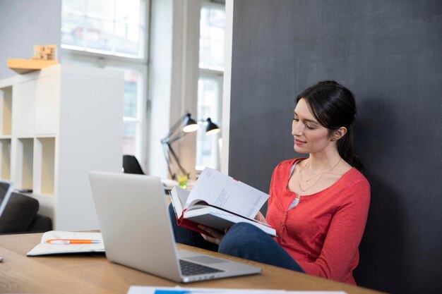 Donna con libro e computer portatile alla scrivania in ufficio