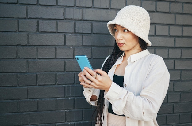 Donna con lo sfondo della parete del telefono e streetwear che digita sui social media post chat o ricerca su Internet Ragazza di moda urbana gen z o influencer online con smartphone per la creazione di contenuti e tecnologia