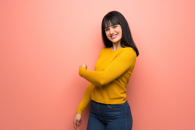 Donna con maglione giallo sulla parete rosa che punta indietro