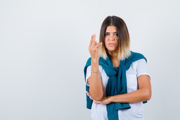 Donna con maglione legato in maglietta bianca che fa il segno della pistola con il dito e sembra sicura, vista frontale.