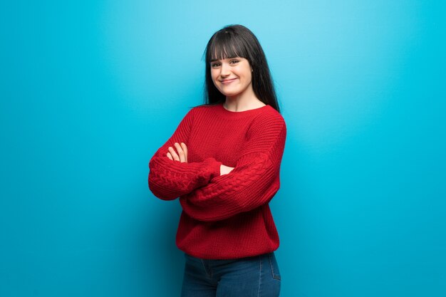 Donna con maglione rosso sulla parete blu con le braccia incrociate e guardando avanti