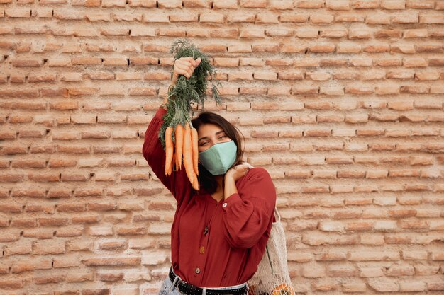 Donna con maschera facciale all'aperto tenendo le carote