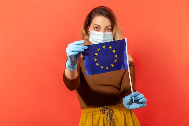 Donna con maschera igienica e guanti che mostrano il concetto di bandiera dell'Unione europea della minaccia pandemica del coronavirus in Europa abolizione dei visti e restrizioni di viaggio alle frontiere chiuse, ripresa in studio al coperto isolata