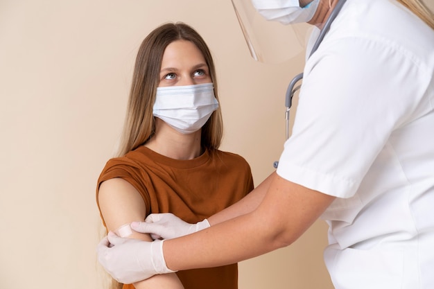 Donna con maschera medica che riceve un adesivo sul braccio dopo aver ricevuto un vaccino