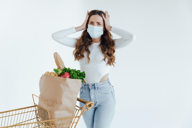 Donna con maschera medica che tiene una borsa della spesa piena di cibo fresco.