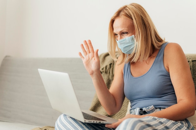 Donna con maschera medica e laptop a casa