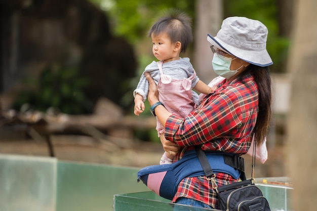 Donna con maschera medica per proteggere il coronaviruscovid19 mentre tiene il bambino nello zoo