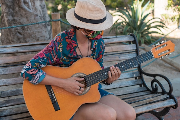 Donna con maschera protettiva che suona la sua chitarra acustica