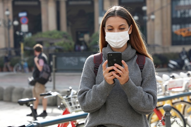 Donna con maschera protettiva utilizzando smartphone e guardando in mostra nel centro della città