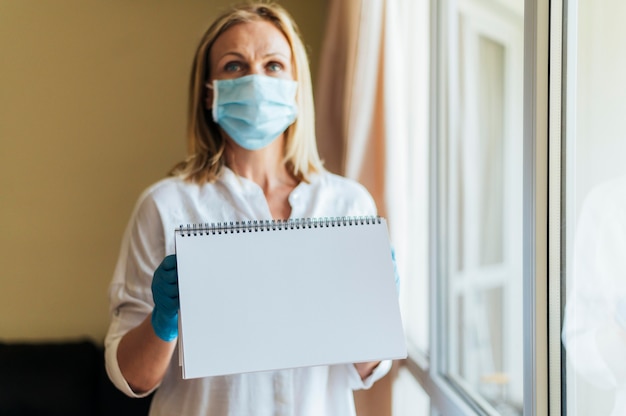 Donna con mascherina medica a casa tenendo il taccuino