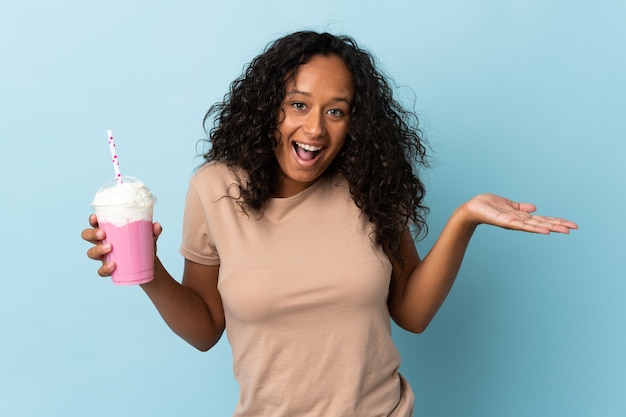 Donna con milkshake alla fragola isolato sul blu con l'espressione facciale scioccata