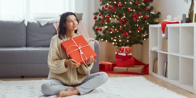 Donna con regalo nella confezione regalo vicino all'albero di Natale a casa