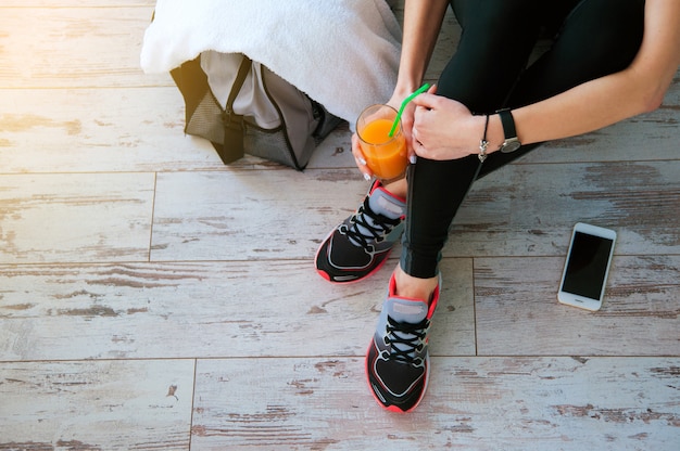 Donna con seduta sul pavimento con un bicchiere di succo d&#39;arancia dopo lo sport