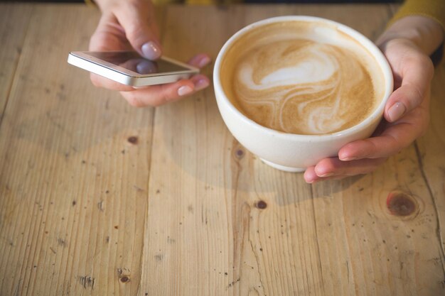 Donna con smartphone seduto in un bar all'aperto e bere caffè