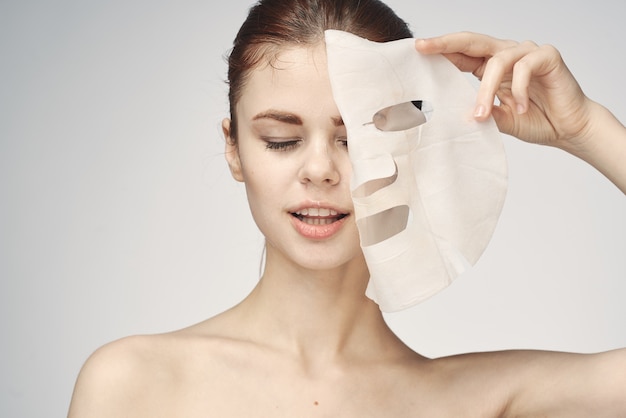 Donna con spalle nude e cosmetici per la cura della pelle con maschera facciale