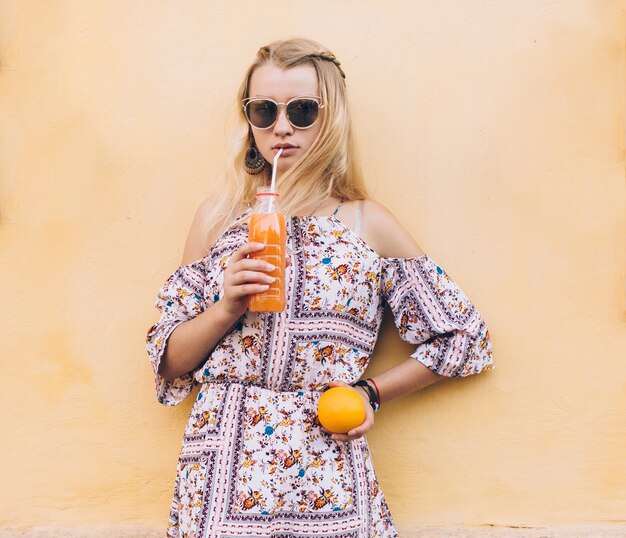 Donna con succo e arancia al muro