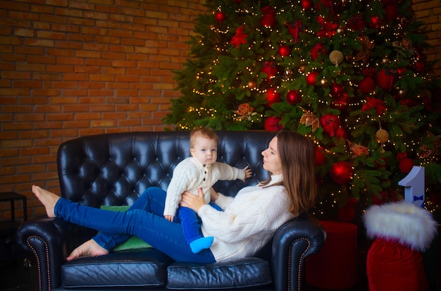 Donna con suo figlio bambino vicino a un albero di Natale in un interno buio.